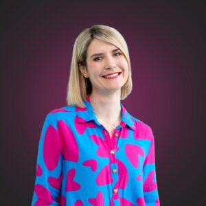 Janina Bąk, młoda kobieta blondynka, uśmiecha się, ubrana w kolorową koszule
