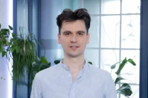 Piotr Latała, młody mężczyzna w białej koszuli rozpiętej pod szyją